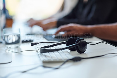 Buy stock photo Shot of a set of headsets lying on a desk with workers sitting in the background