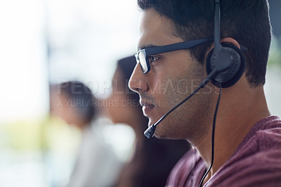 Buy stock photo Shot of a young man wearing a headset with his colleagues blurred in the background