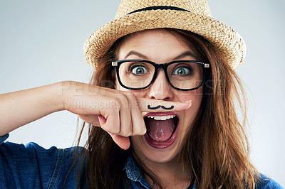 Buy stock photo Studio portrait of a young woman holding her finger under her nose with a moustache drawn on it