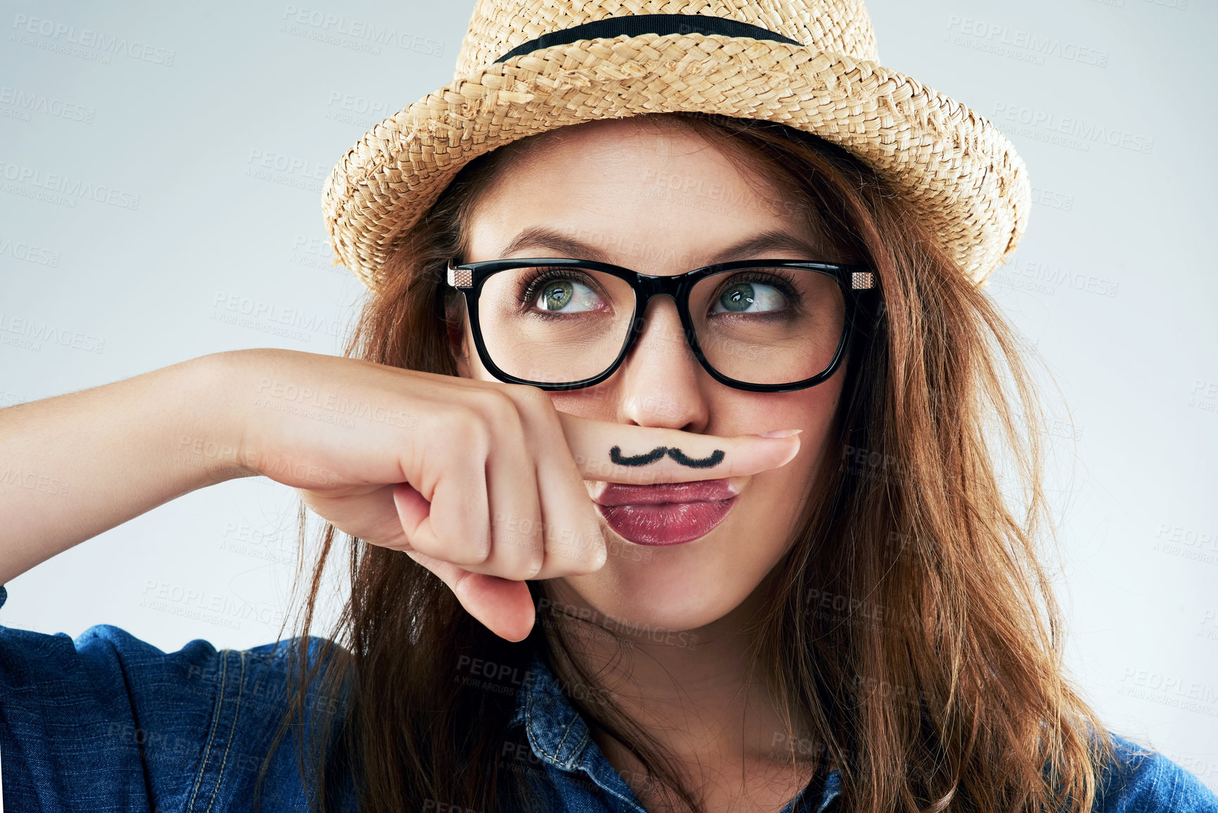 Buy stock photo Studio shot of a young woman holding her finger under her nose with a moustache drawn on it