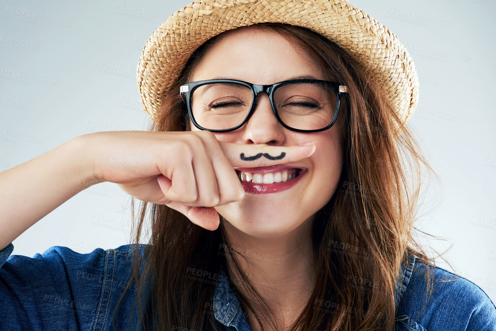 Buy stock photo Studio shot of a young woman holding her finger under her nose with a moustache drawn on it