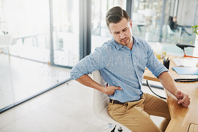 Buy stock photo Cropped shot of a young businessman experiencing back pain while working at his desk