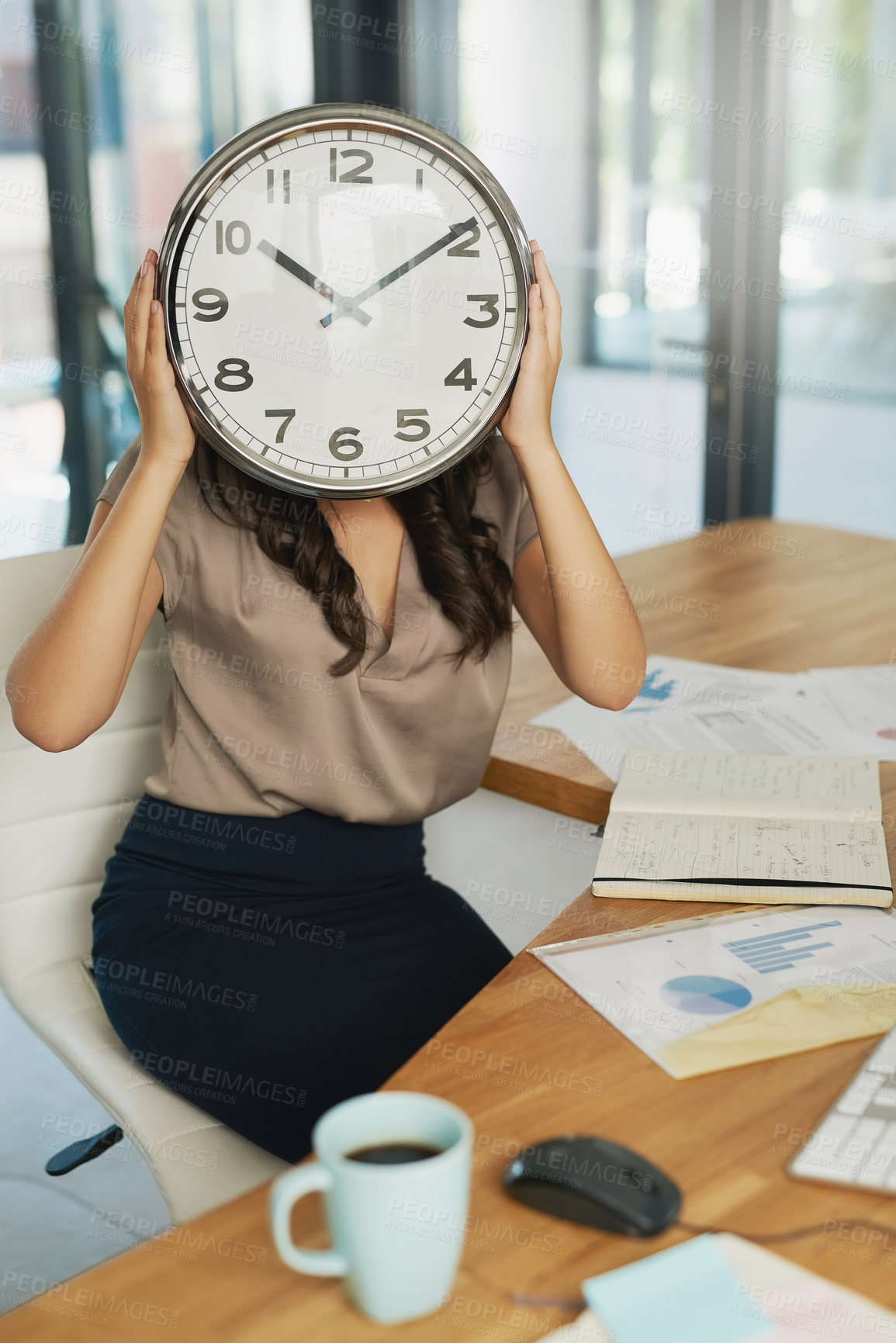 Buy stock photo Shot of an unidentifiable businesswoman holding a clock in front of her face while sitting at her desk
