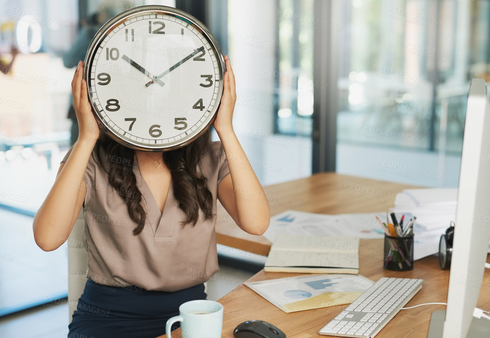 Buy stock photo Shot of an unidentifiable businesswoman holding a clock in front of her face while sitting at her desk