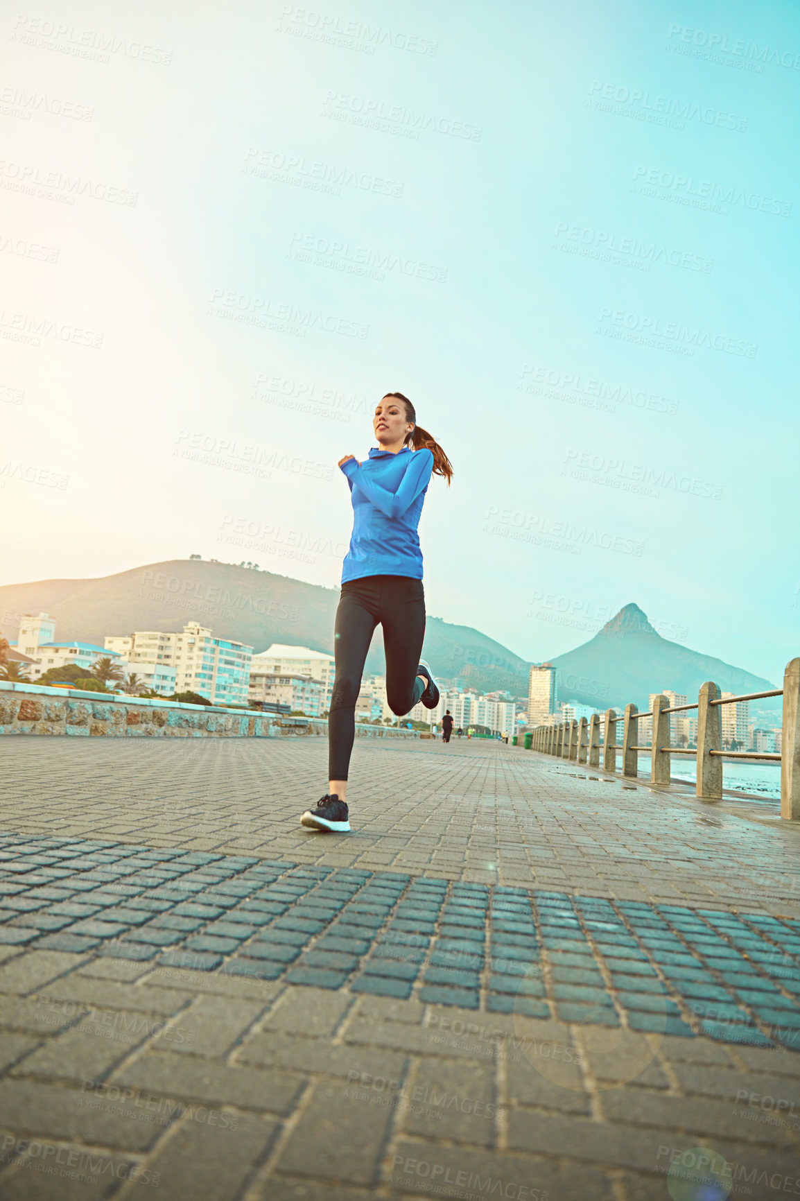 Buy stock photo Shot of a sporty young woman out running on the promenade