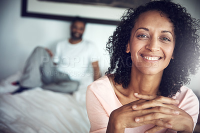 Buy stock photo Portrait of a happy mature woman sitting on the edge of the bed with her husband in the background