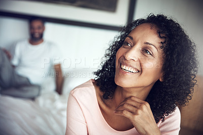 Buy stock photo Shot of a happy mature woman sitting on the edge of the bed with her husband in the background