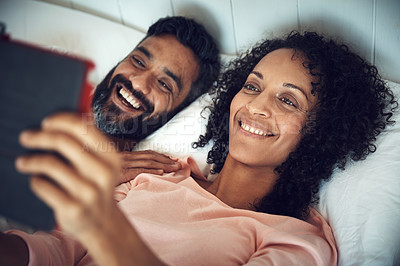 Buy stock photo Shot of a mature couple using a digital tablet while relaxing together in bed