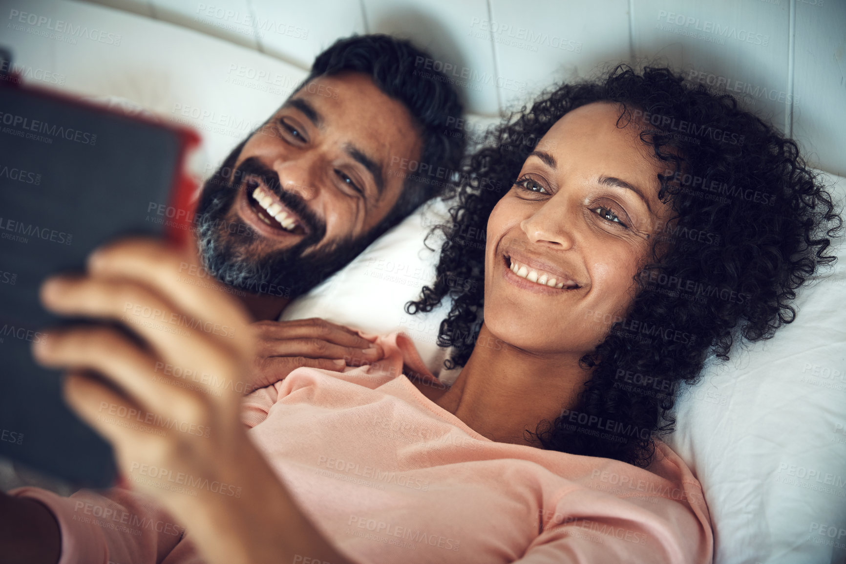 Buy stock photo Shot of a mature couple using a digital tablet while relaxing together in bed