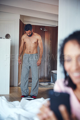 Buy stock photo Shot of a mature man weighing himself on a scale with his wife in the foreground