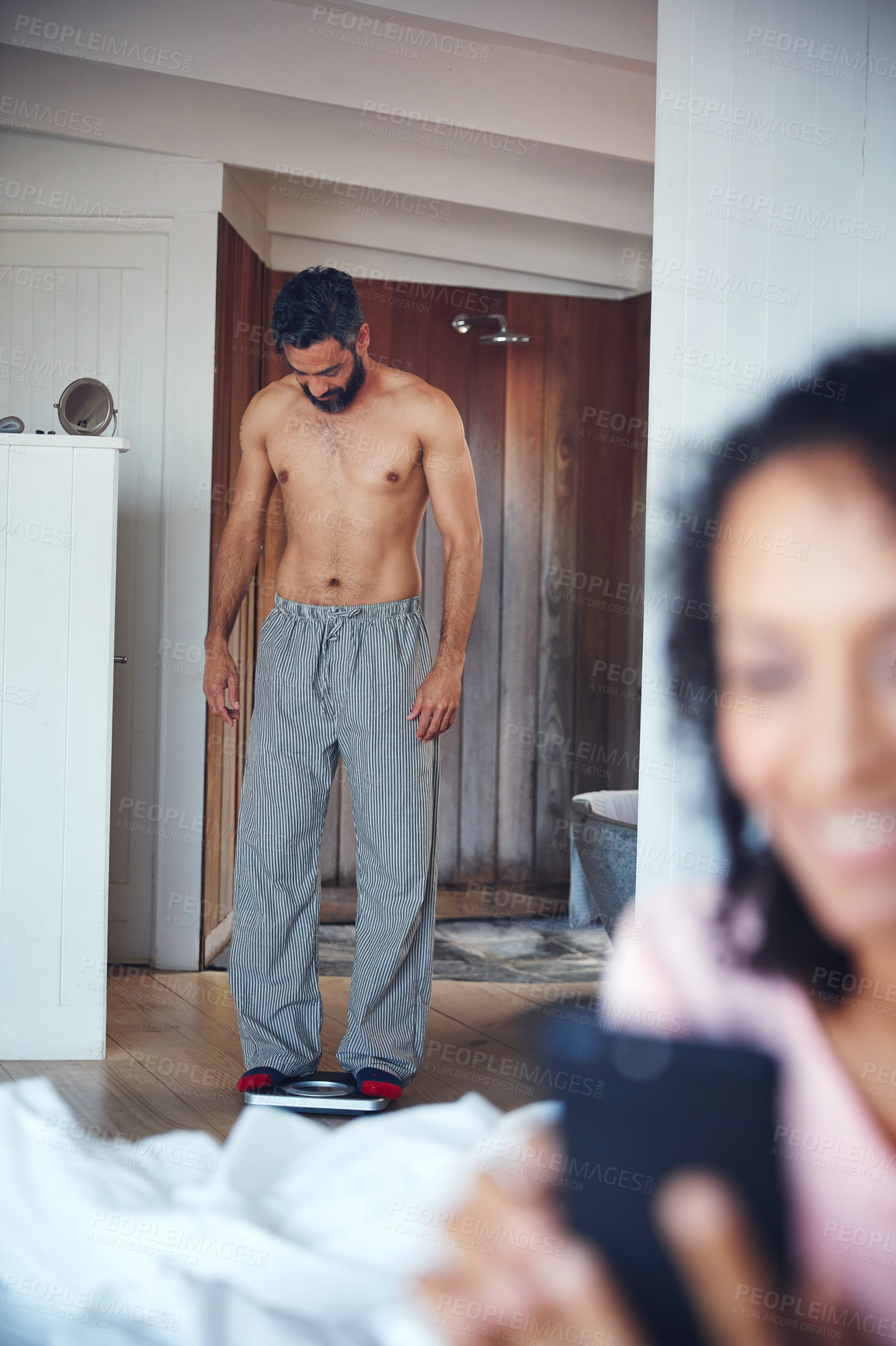 Buy stock photo Shot of a mature man weighing himself on a scale with his wife in the foreground