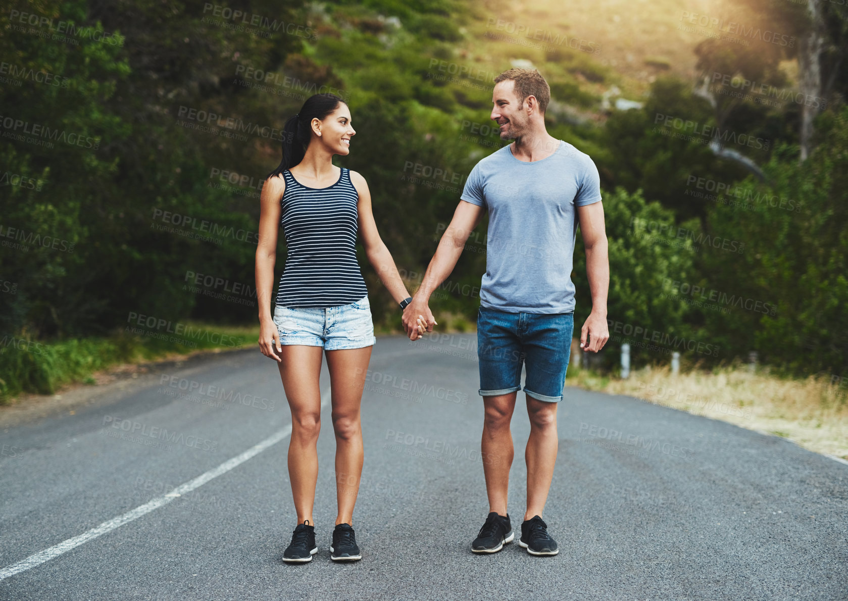 Buy stock photo Shot of a happy young couple walking down a road outside