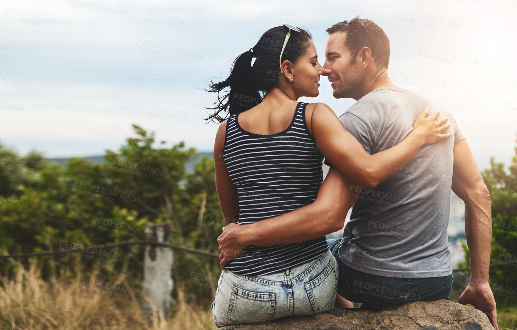 Buy stock photo Back view, love or happy couple hug in park for date, freedom or care in nature with peace or bond. Eye contact, romantic man or woman on rock or outdoor holiday vacation together to relax or travel