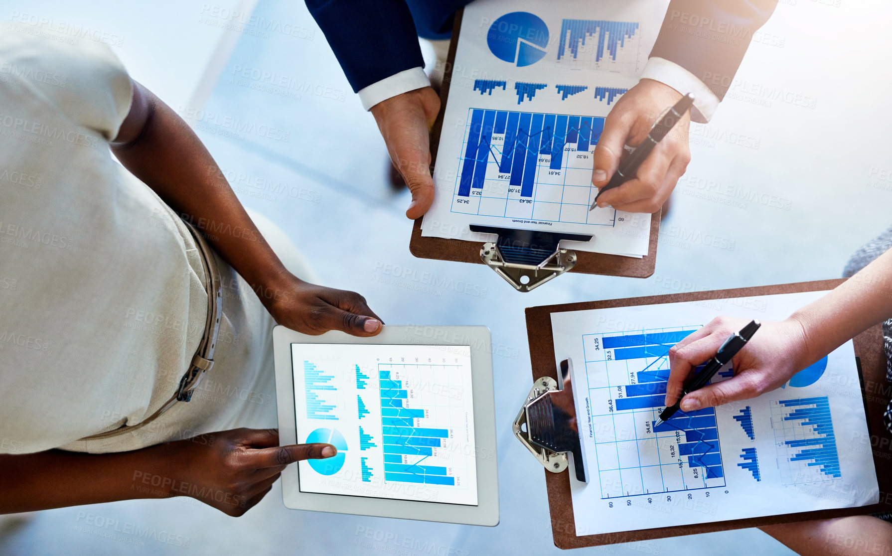 Buy stock photo High angle shot of a group of unidentifiable businesspeople looking at graphs on a tablet in the office