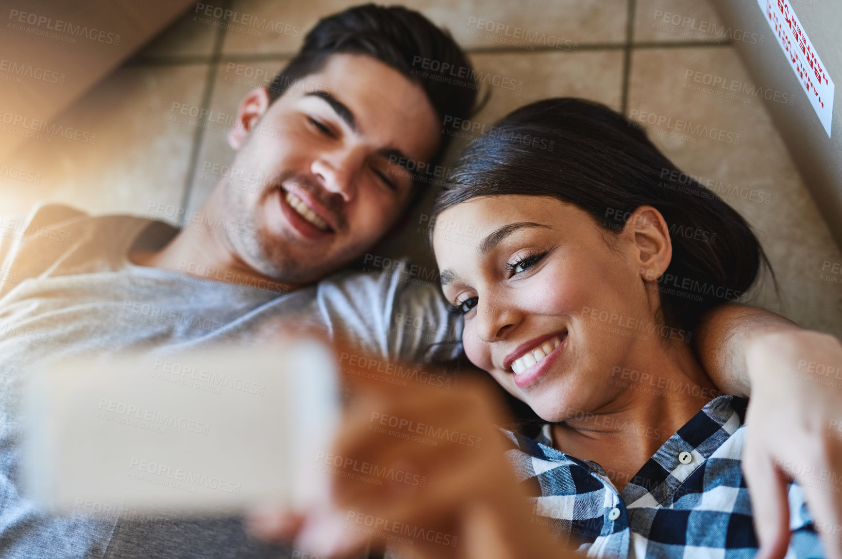 Buy stock photo Shot of a happy young couple taking a selfie while lying on the floor of their new home