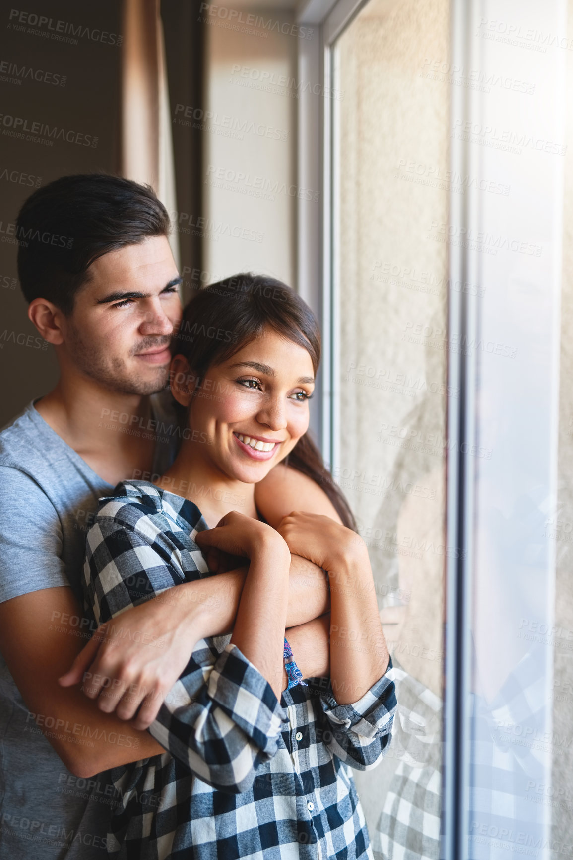 Buy stock photo Couple, hug and window of home for peace, support and bonding on weekend for relationship. People, reflection and embrace for security in connection, relax and together for date on trip for marriage