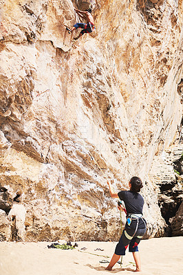 Buy stock photo Shot of two young people rock climbing on a sunny day