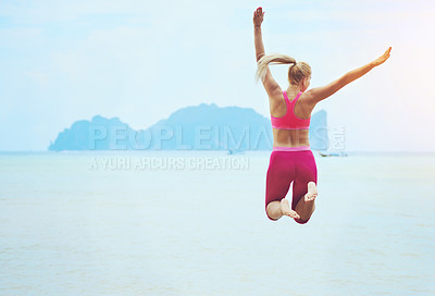 Buy stock photo Rearview shot of a sporty young woman jumping into the air on a tropical beach