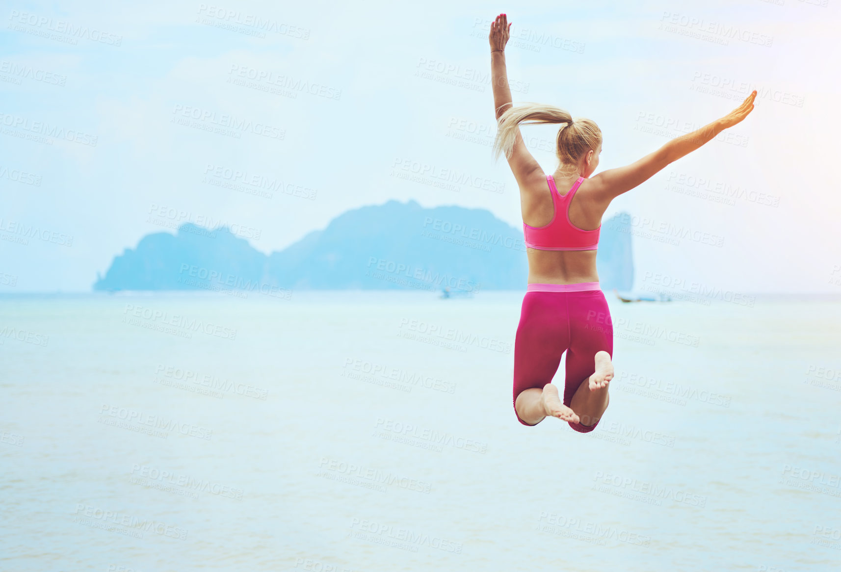 Buy stock photo Rearview shot of a sporty young woman jumping into the air on a tropical beach