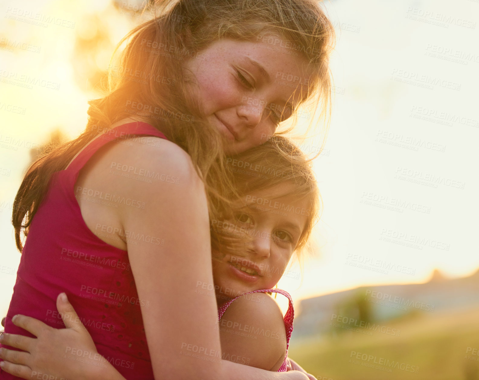 Buy stock photo Shot of a sweet little girl giving her sister a hug while they play in the park