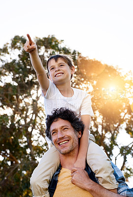 Buy stock photo Shot of a happy boy pointing at something while being carried by his father outdoors