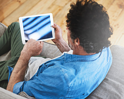 Buy stock photo Rearview shot of a bachelor relaxing on the sofa with his tablet