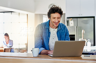 Buy stock photo Shot of a happy man using his laptop while sitting in the kitchen