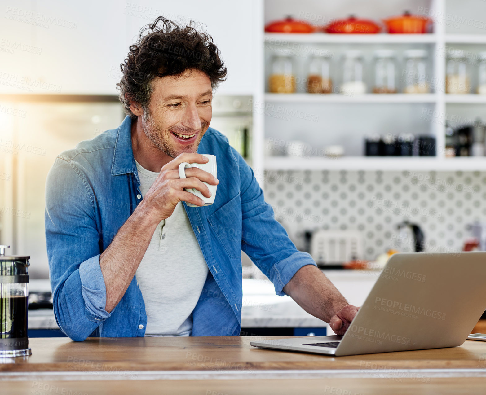 Buy stock photo Shot of a bachelor using his laptop while enjoying a cup of coffee in the kitchen