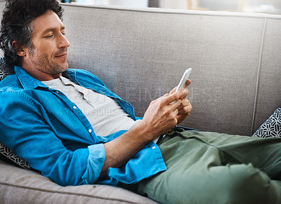Buy stock photo Shot of a bachelor relaxing on the sofa with his smartphone