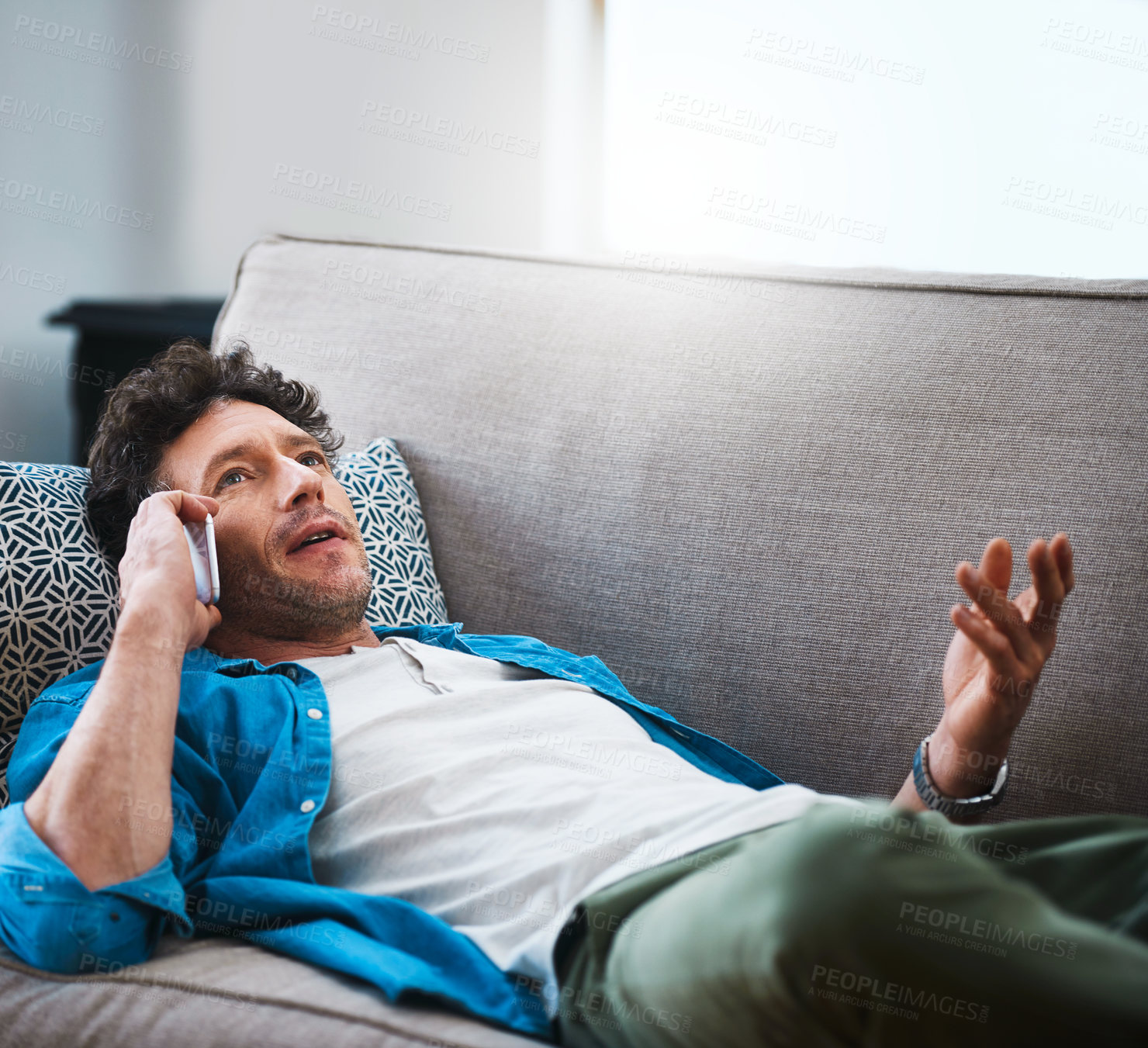 Buy stock photo Man, relax and talking with phone on sofa for conversation, communicatin or chat in living room at home. Young male person lying on couch with mobile smartphone for friendly discussion at house