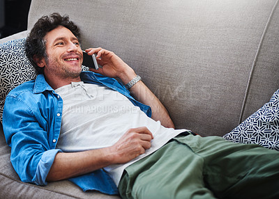 Buy stock photo Shot of a happy bachelor answering his cellphone while relaxing on the couch at home