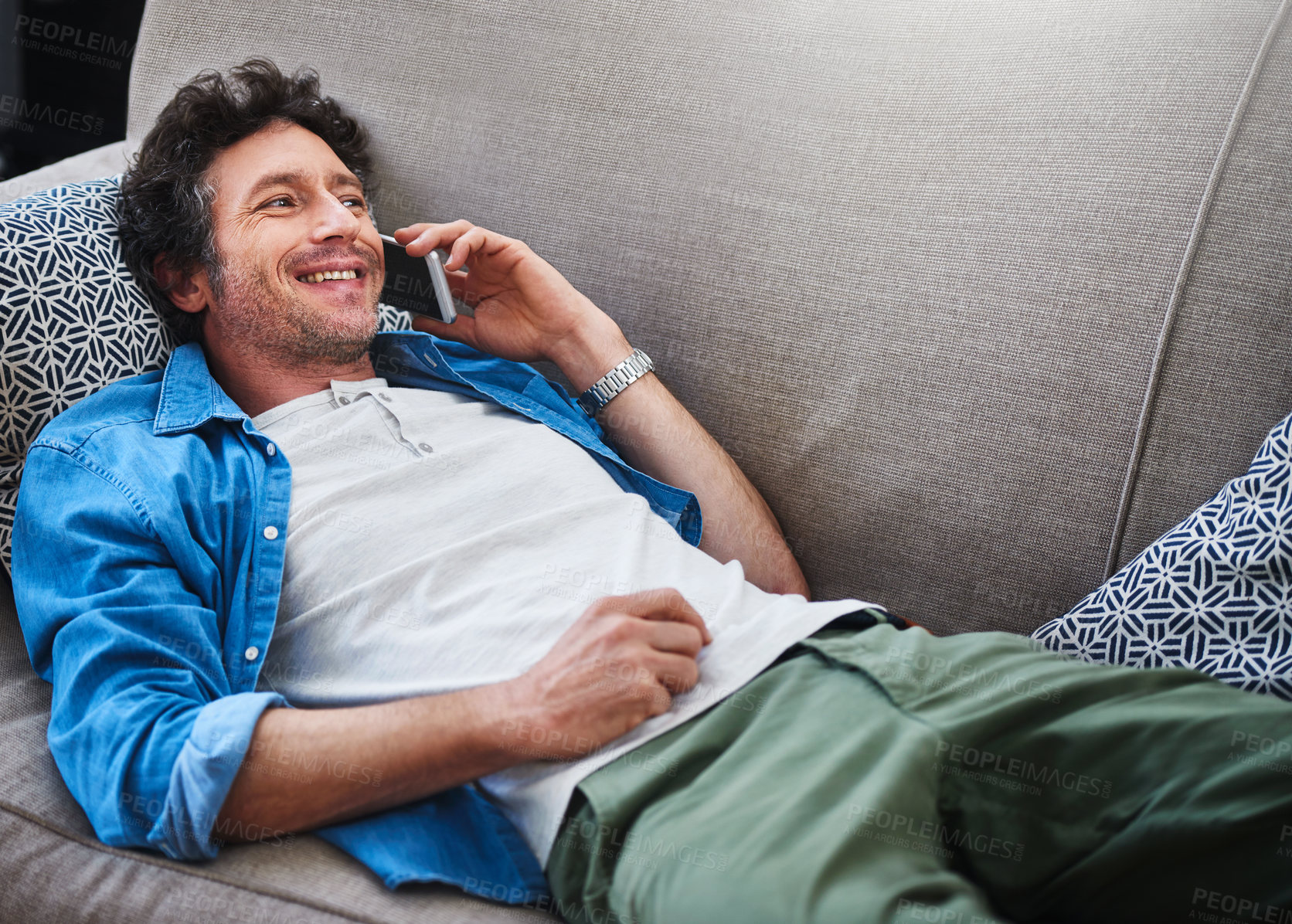Buy stock photo Shot of a happy bachelor answering his cellphone while relaxing on the couch at home