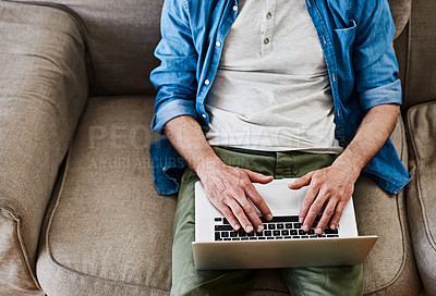 Buy stock photo High angle shot of an unidentifiable bachelor using his laptop while relaxing on the couch