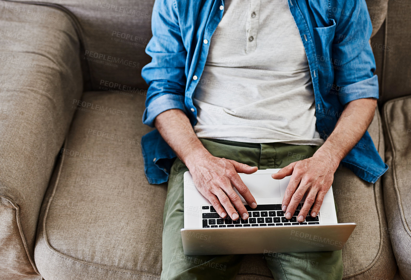 Buy stock photo High angle shot of an unidentifiable bachelor using his laptop while relaxing on the couch