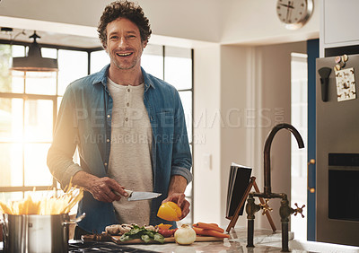 Buy stock photo Portrait of a happy bachelor chopping vegetables in his kitchen