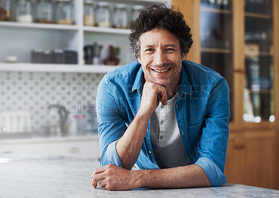 Buy stock photo Portrait of a happy bachelor leaning on his kitchen counter