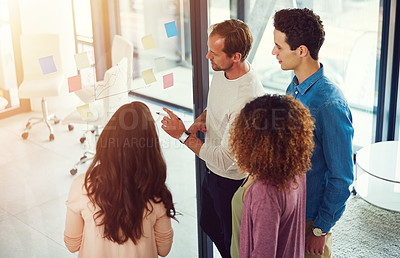 Buy stock photo Cropped shot of a group of young designers brainstorming with notes on a glass wall in an office