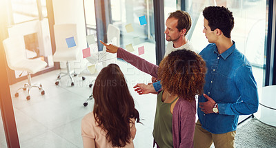 Buy stock photo Cropped shot of a group of young designers brainstorming with notes on a glass wall in an office