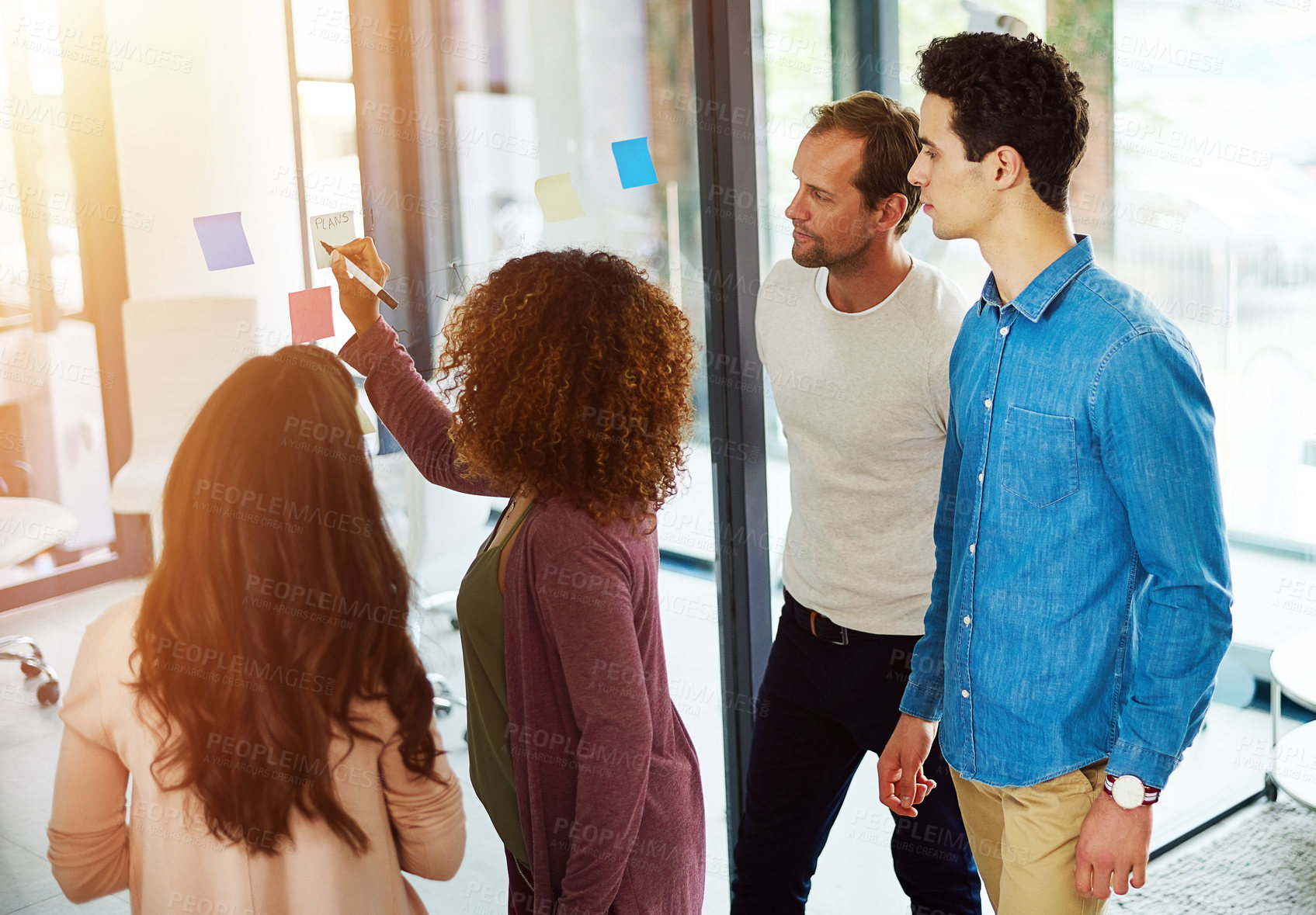 Buy stock photo Cropped shot of a group of young designers brainstorming with notes on a glass wall in an office