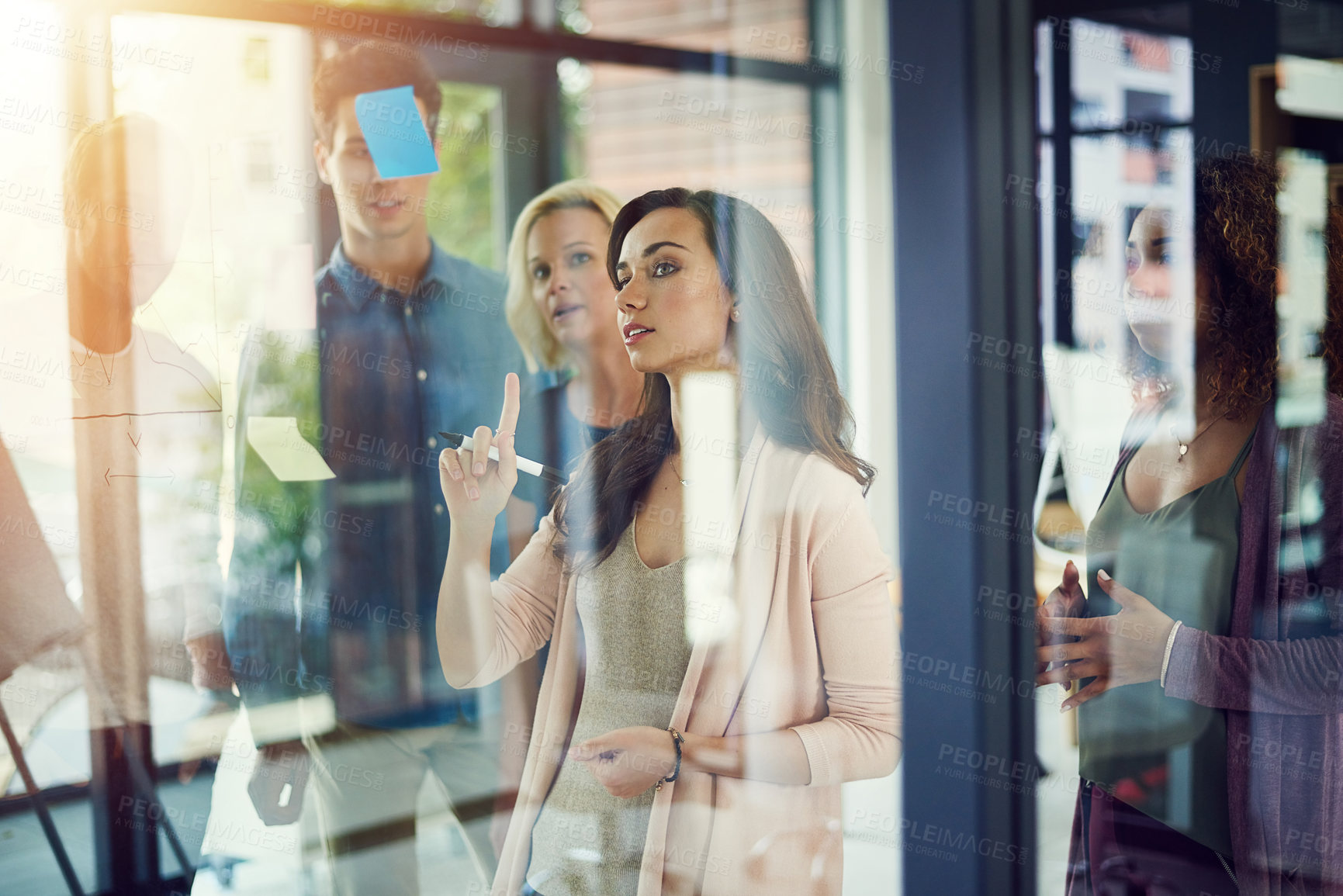 Buy stock photo Cropped shot of a group of young designers brainstorming with notes on a glass wall in an office