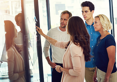 Buy stock photo Cropped shot of a group of young designers brainstorming with notes on a glass wall in an office