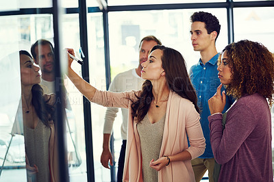 Buy stock photo Cropped shot of a group of young designers brainstorming with notes on a glass wall in an office