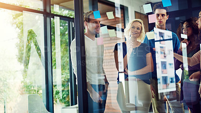 Buy stock photo Cropped shot of a group of young designers brainstorming with notes on a glass wall in an office