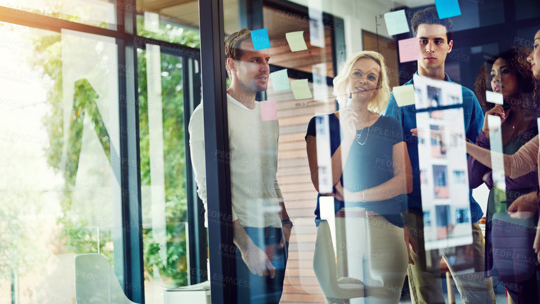 Buy stock photo Cropped shot of a group of young designers brainstorming with notes on a glass wall in an office