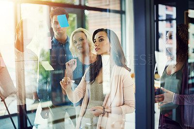 Buy stock photo Cropped shot of a group of young designers brainstorming with notes on a glass wall in an office