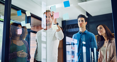 Buy stock photo Cropped shot of a group of young designers brainstorming with notes on a glass wall in an office