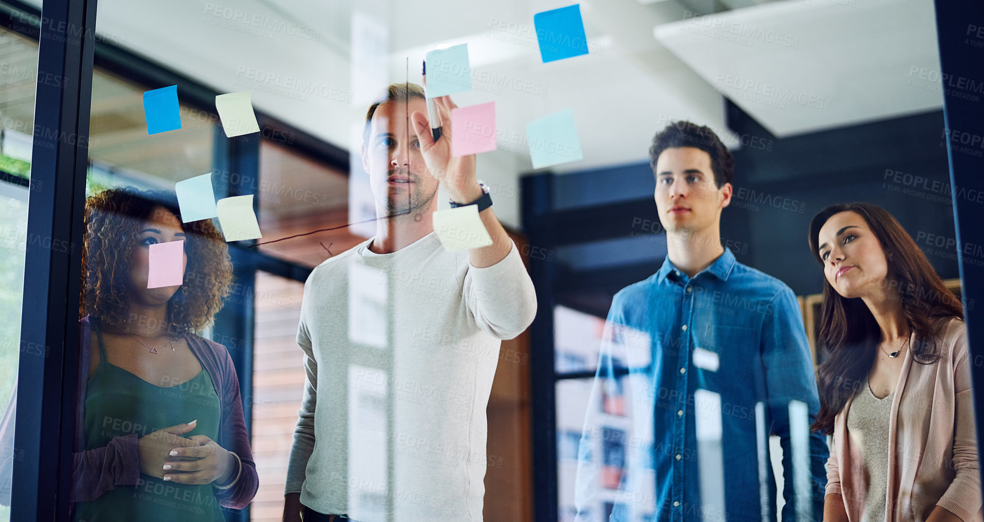 Buy stock photo Cropped shot of a group of young designers brainstorming with notes on a glass wall in an office