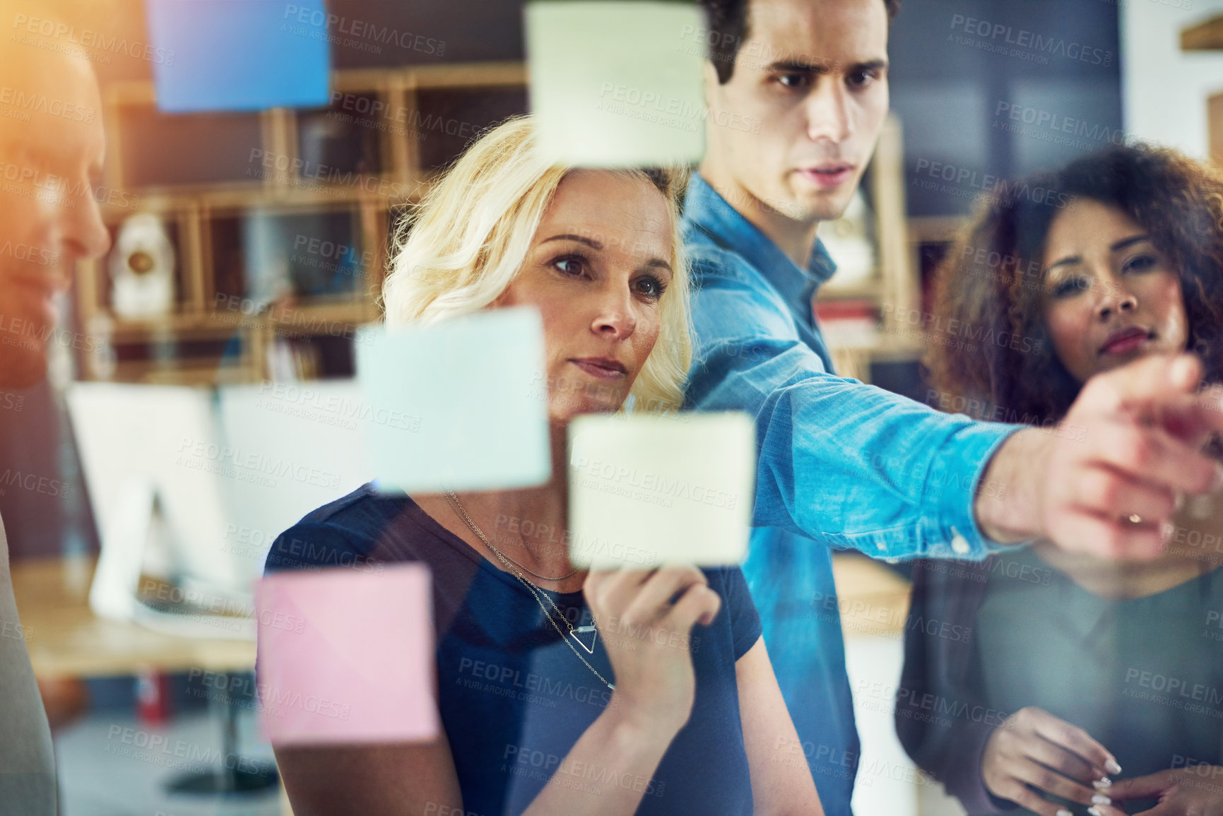 Buy stock photo Cropped shot of a group of young designers brainstorming with notes on a glass wall in an office