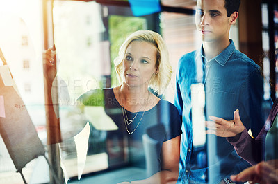 Buy stock photo Cropped shot of a group of young designers brainstorming with notes on a glass wall in an office