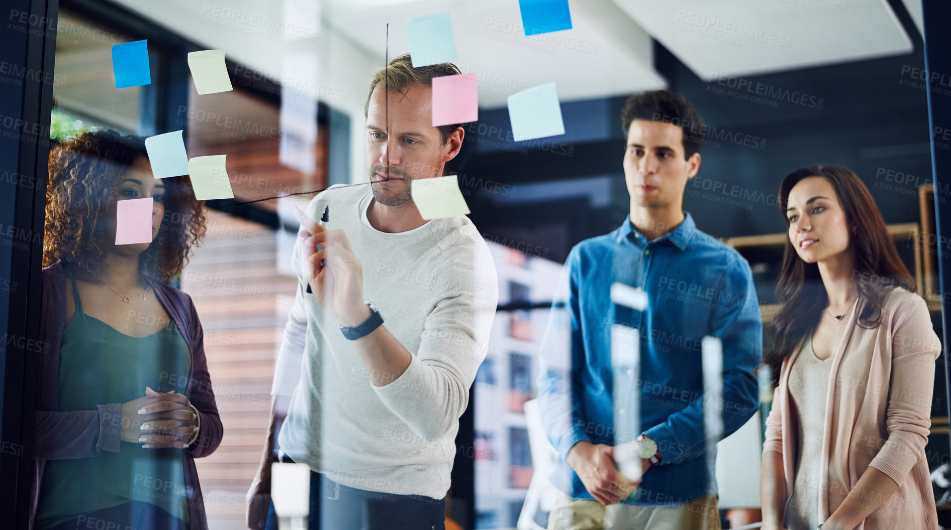 Buy stock photo Cropped shot of a group of young designers brainstorming with notes on a glass wall in an office